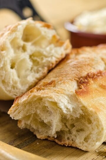 finished mini baguette torn in half on a cutting board with a bowl of butter in the background.