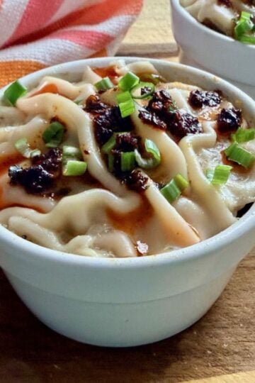 Finished soup dumpling lasagna topped with chili crisp and sliced green onions in individual ramekins.