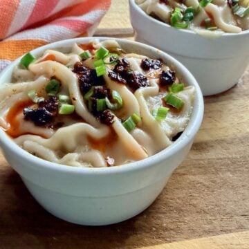 Finished soup dumpling lasagna topped with chili crisp and sliced green onions in individual ramekins.