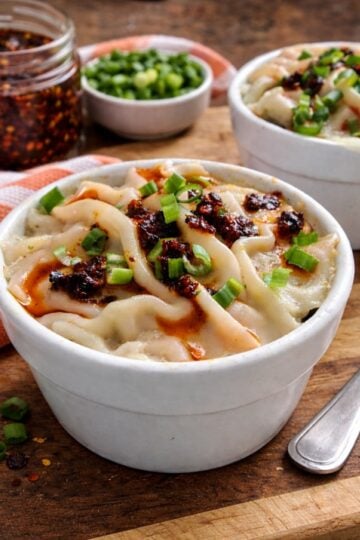 Finished soup dumpling lasagna topped with chili crisp and sliced green onions in individual ramekins.