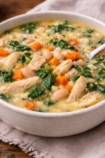 White bowl with chicken and white bean soup and a spoon resting in it