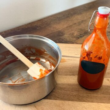 Empty saucepan with a spatula beside a bottle of homemade North Shore barbecue sauce on a wooden cutting board.