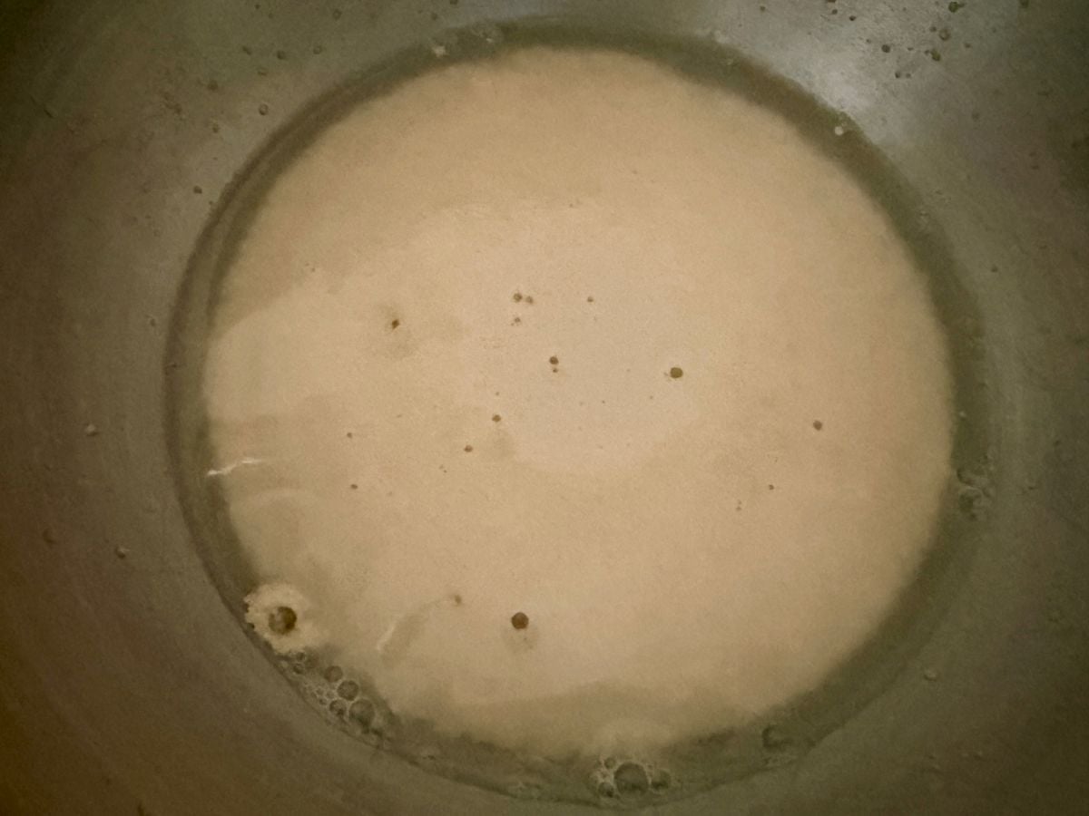 Active dry yeast blooming in warm water and sugar in a glass bowl before mixing onion roll dough.
