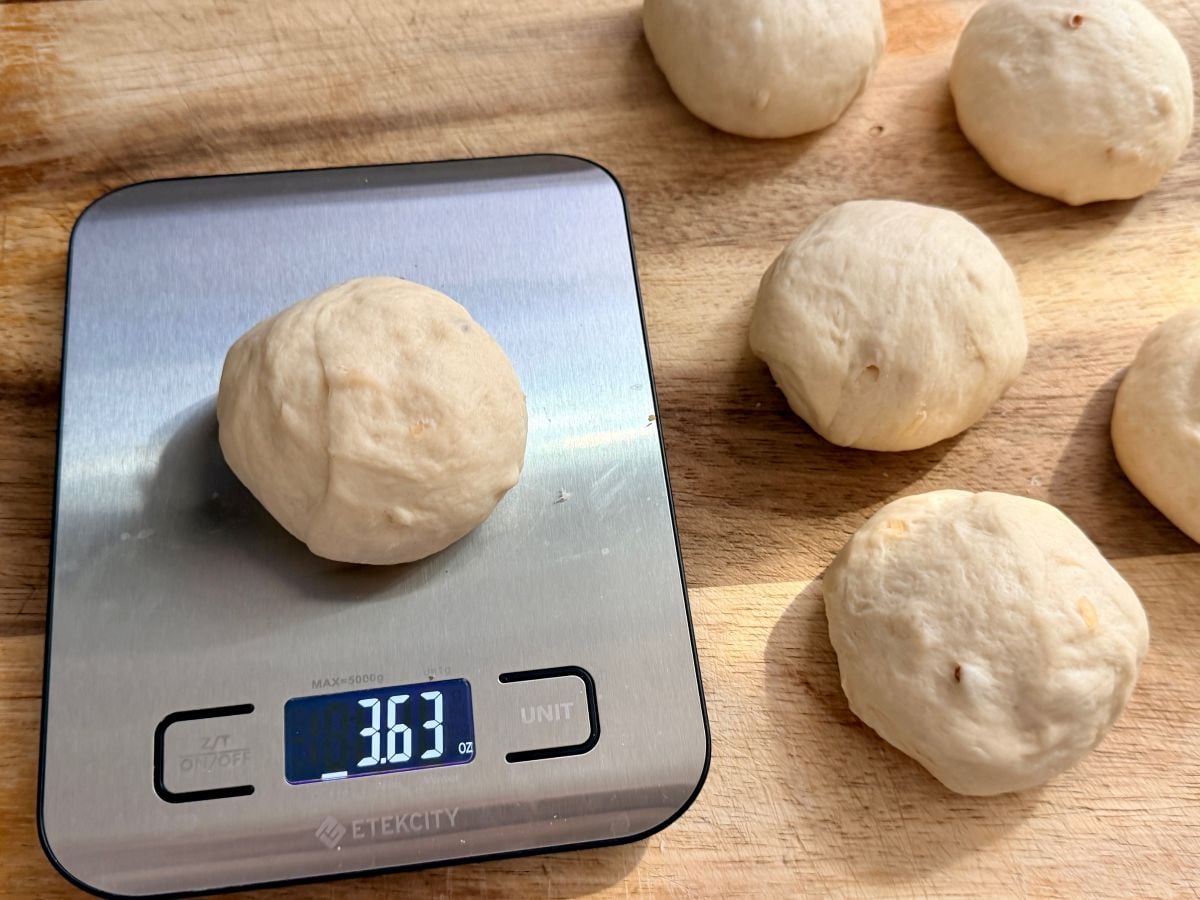Weighing onion roll dough portions on a kitchen scale to make evenly sized homemade sandwich rolls.