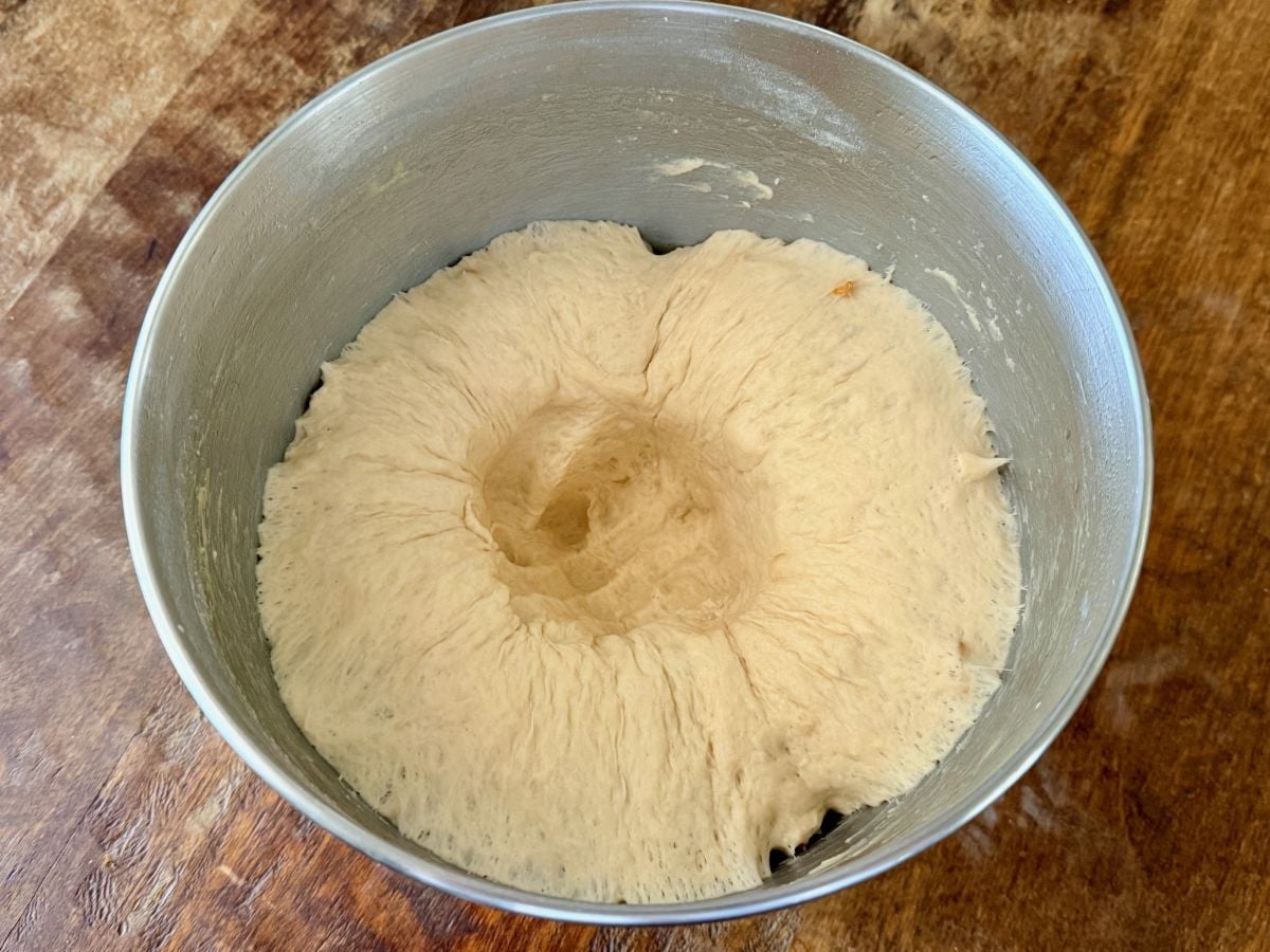 Punching down risen onion roll dough in a mixing bowl before dividing and shaping.