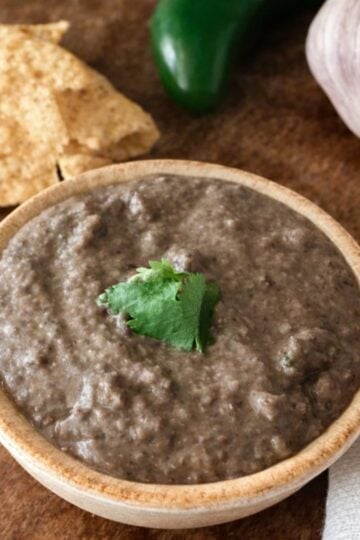 creamy restaurant-style black bean dip served with tortilla chips with a jalapeno and garlic head in the background