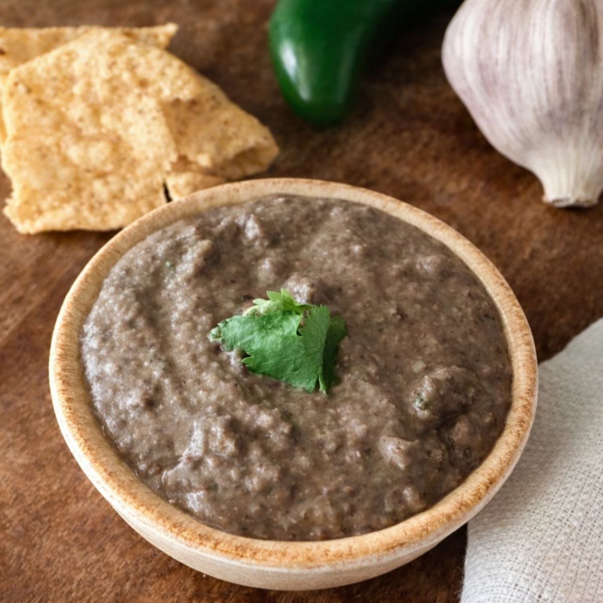creamy restaurant-style black bean dip served with tortilla chips with a jalapeno and garlic head in the background
