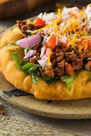 Navajo taco with all of the toppings on a rustic plate