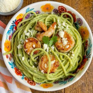 Grilled shrimp served over creamy green spaghetti made with a roasted poblano and jalapeño cream sauce, topped with crumbled queso fresco and fresh cilantro in a colorful floral bowl.
