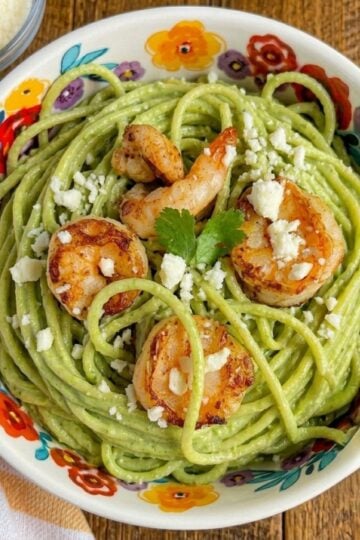 Grilled shrimp served over creamy green spaghetti made with a roasted poblano and jalapeño cream sauce, topped with crumbled queso fresco and fresh cilantro in a colorful floral bowl.