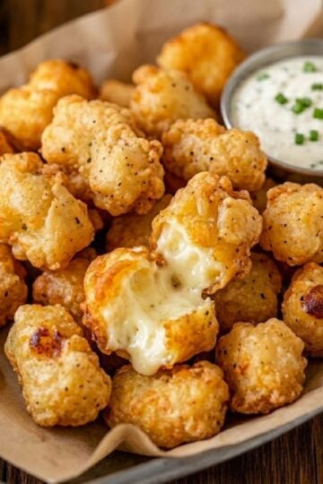 Crispy Wisconsin fried cheese curds served in a metal basket with jalapeño ranch dipping sauce and a gooey cheese pull.