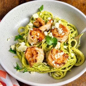 Green spaghetti with shrimp topped with queso fresco and cilantro in a serving bowl.