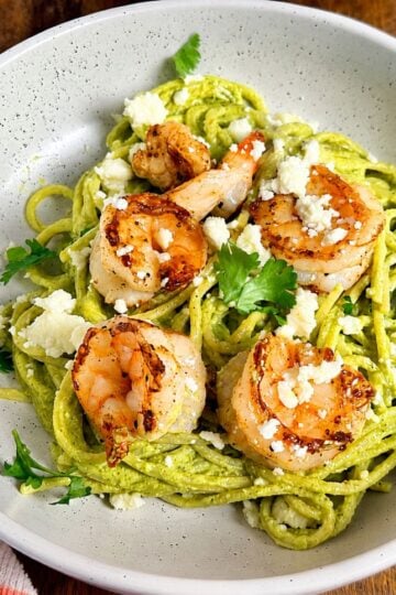 Green spaghetti with shrimp topped with queso fresco and cilantro in a serving bowl.