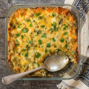 Baked green chile chicken enchilada casserole topped with melted cheese and fresh cilantro in a glass baking dish.