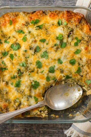 Baked green chile chicken enchilada casserole topped with melted cheese and fresh cilantro in a glass baking dish.
