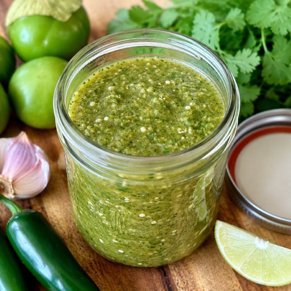Homemade roasted salsa verde stored in a mason jar with fresh tomatillos, jalapeños, cilantro, garlic, and lime.